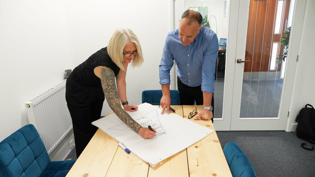 Theresa and Graham talking performance with a pen and paper on a table