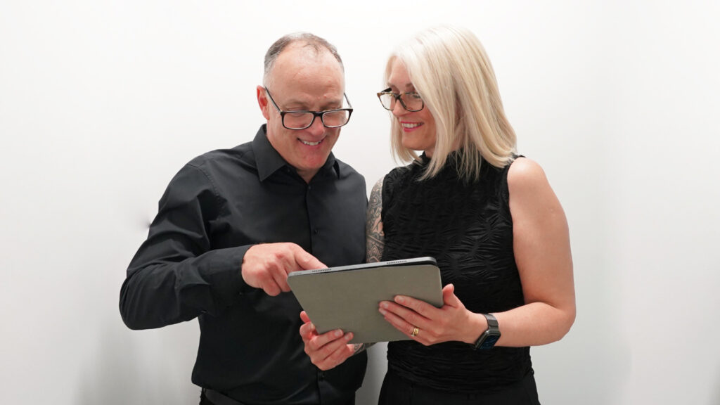 Graham a balding man and Theresa a blonde woman discussing performance