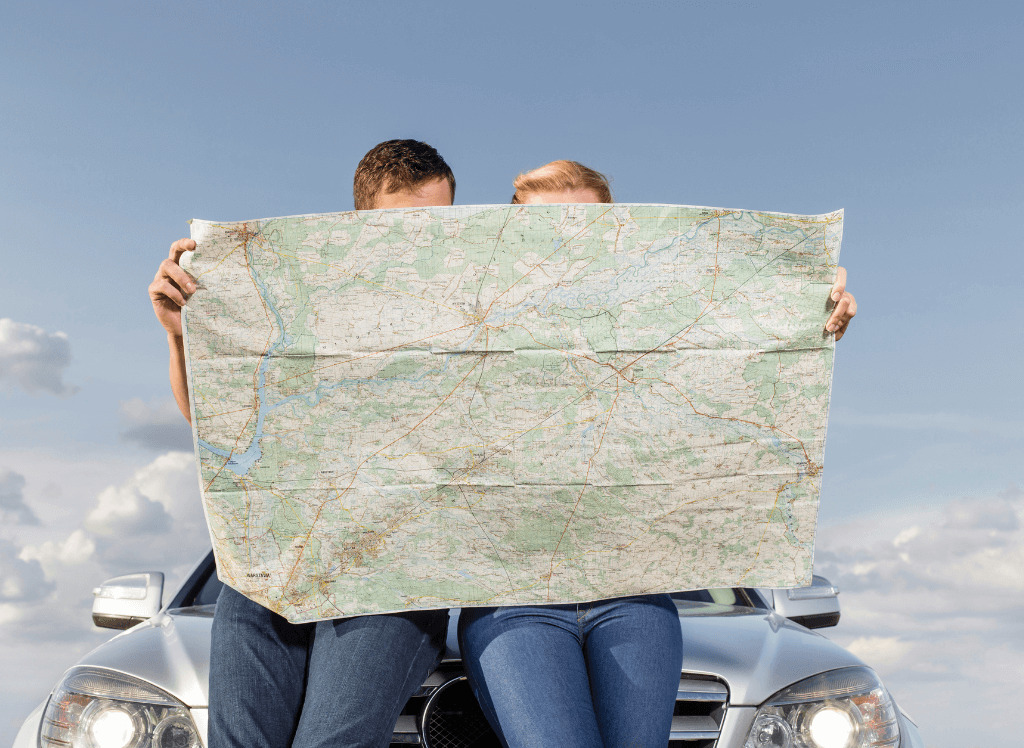 Image shows two people sat on a car bonnet reading a road map